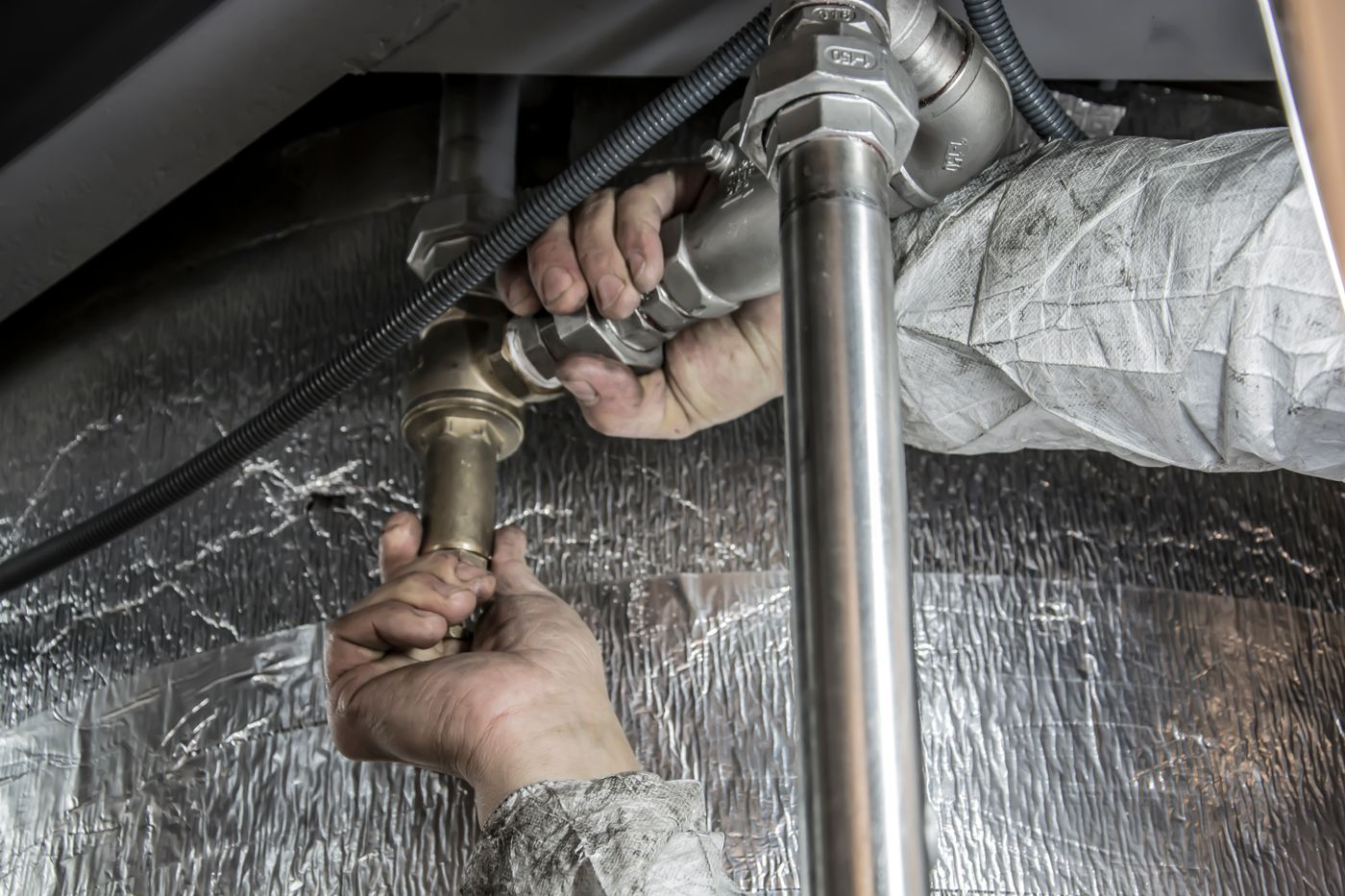 Close-up of two hands tightening a brass fitting on a water supply pipe